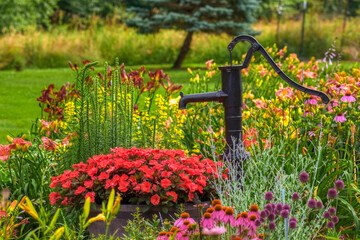 A hand water pump is in the middle of this beautiful home garden in PA.  Flowers surround this hand...