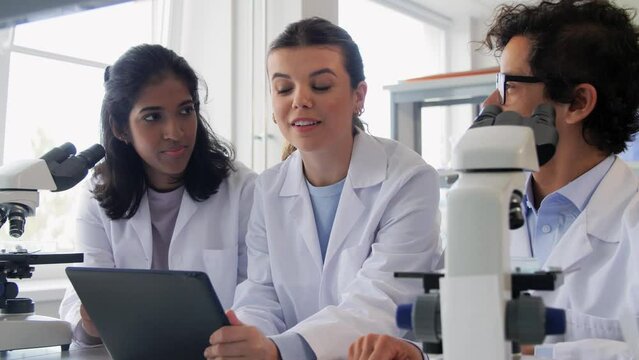 science research, work and people concept - international team of scientists with microscopes and tablet pc computer working in laboratory