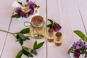 three glass bottles with oil, the essence of natural herbs on a white wooden table among wildflowers. alternative to medicine. selective focus.
