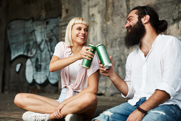 Young smiling couple toasting with beer cans in an urban environment - 517709464