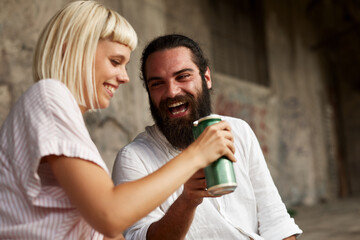 Young smiling couple toasting with beer cans in an urban environment