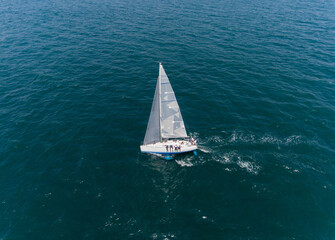 Aerial view a lonely isolated sailboat under the sail with tall mast going in still sea 
