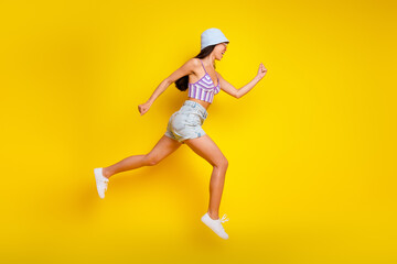 Fototapeta na wymiar Full length photo of adorable hurrying lady wear striped crop top cap jumping high running fast empty space isolated yellow color background