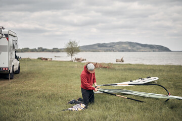 Windsurfer and camper packing and unpacking from a car in nature.