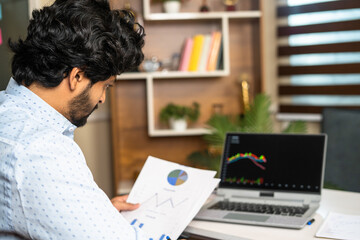 Fototapeta na wymiar young man busy analysing Companies financial charts with technical stock mart charts on laptop - concept of investment, trading and money management