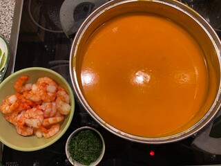 Pumpkin soup being prepared in a pot with side dishes of prawns and herbs - Kürbissuppe im Topf