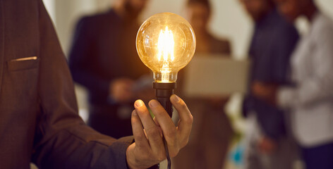 Man holding lightbulb. Human hand holding glowing electric Edison light bulb as symbol of creative...