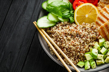 quinoa salad with grilled chicken and vegetables on a black wooden rustic background
