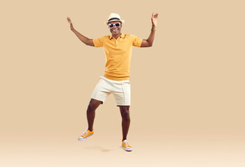 Fototapeta na wymiar Cool cheerful african american man funny rejoicing and dancing isolated on beige background. Emotional dark-skinned man in stylish summer clothes having fun on vacation. Fun concept. Full length.