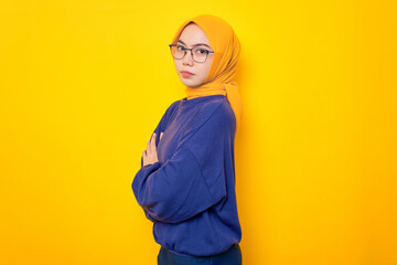 Annoyed young Asian Muslim woman dressed in casual sweater crossed arms and looking at camera isolated over yellow background
