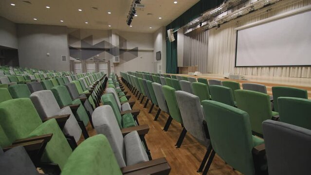 Comfortable chairs and projection screen on stage in empty conference hall in modern business center close view