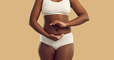 Woman demonstrates gesturing balance in microflora isolated on white background on beige background. Dark skinned plus size model dressed in lingerie holding her hands in circle around her belly.