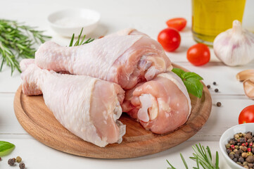 Raw uncooked chicken legs on a cutting board on a white wooden background. Meat with ingredients for cooking