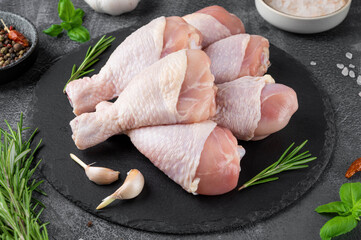 Raw uncooked chicken legs on a dark slate on a dark concrete background. Meat with ingredients for...