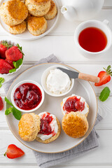 Homemade British Scones with cream cheese, strawberry jam and a cup of tea on a white wooden background.