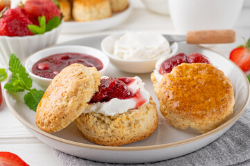 Homemade British Scones with cream cheese, strawberry jam and a cup of tea on a white wooden background.