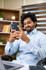 happy Young corporate employee busy using mobile phone at office in front of laptop at desk - concept of relaxation, taking break and social media