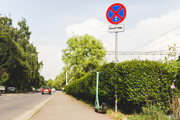 Electric scooter parked near a sign that is not allowing parking for vehicles otherwise the car...