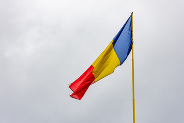 Romanian flag waving against a cloudy sky on a yellow pillar or stick