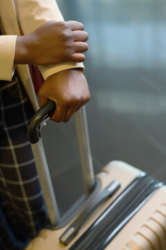 Hands of young elegant black woman holding by handle of suitcase with luggage while standign in hotel lounge and waiting for bellboy