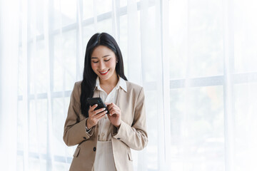 Obraz premium Portrait of elegant successful asian business woman speaking by smartphone and smiling happily while standing against window in office.