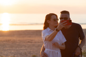 Happy couple with age difference - a young woman and a middle aged man take a selfie on the beach