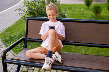 The boy is sitting on a bench and looking at the phone