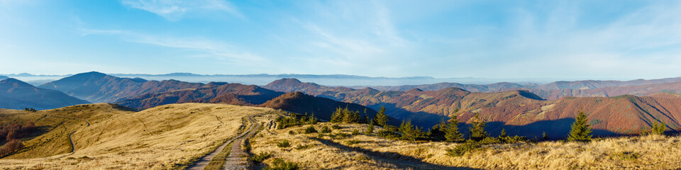 Rural road in autumn mountain and colorful trees on slopes. Morning panorama view.