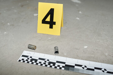 Fototapeta premium Yellow card with number four standing on asphalt by two empty cartridge cases left on crime scene shot from handgun of murderer