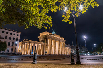 Illuminated Brandenburg Gate at night from the west side framed by trees and lamps - Oblique wide 