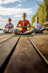 Group of senior woman doing yoga exercises by the lake.