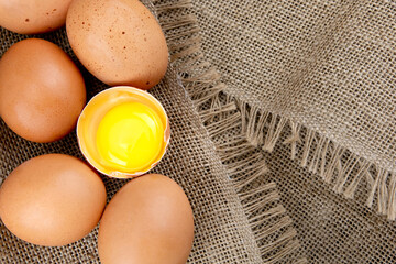 Fresh chicken brown eggs on burlap background, broken raw egg, top view