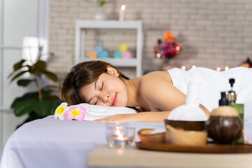 Obraz na płótnie Canvas Asian woman lying in bed doing spa with smiling, happy, relaxing face in candlelight. warm atmosphere with her facing the camera