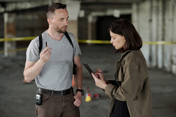 Confident detective inspector and his female colleague discussing evidences or circumstances of murder during crime scene investigation