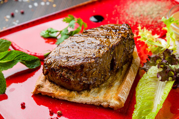 juicy Striploin Steak on red plate with bread and vegetables