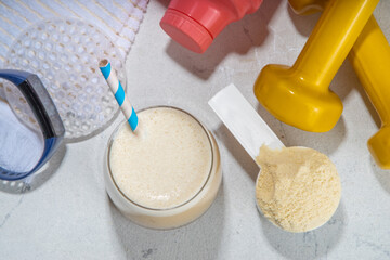 Vanilla white protein shake glass, with straw, with protein powder, dumbbell, towel and fitness accessories, on white sport bar table background copy space