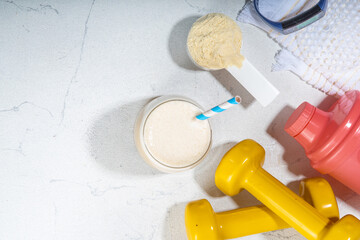Obraz na płótnie Canvas Vanilla white protein shake glass, with straw, with protein powder, dumbbell, towel and fitness accessories, on white sport bar table background copy space