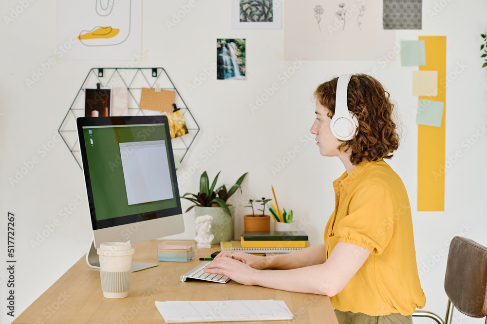 Poster Side view of young modern freelancer typing on computer keyboard while sitting in front of monitor with small blank window