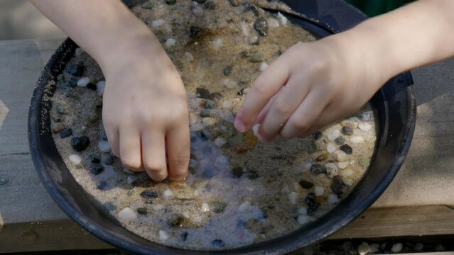 Children using gold pans to look for gems in sand in slow motion