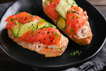 Sandwiches. Salmon toast with cream cheese, cucumber, black sesame and microgreens on old wooden table background. Seafood. Healthy food. Photography in low key. Top view.