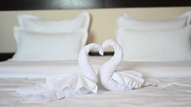 Swans made of white bath towel in hotel room. Decoration on bed in motel. Towel folded in swan shape. 