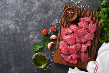 Raw chopped beef meat. Raw organic meat beef or lamb, spices, herbs on old wooden board on dark grey concrete background. Goulash. Raw uncooked meat. Meat with blood. Top view with copy space.
