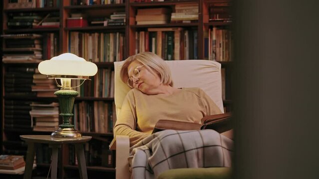 Tired senior woman fell asleep while reading in a home library, retirement life