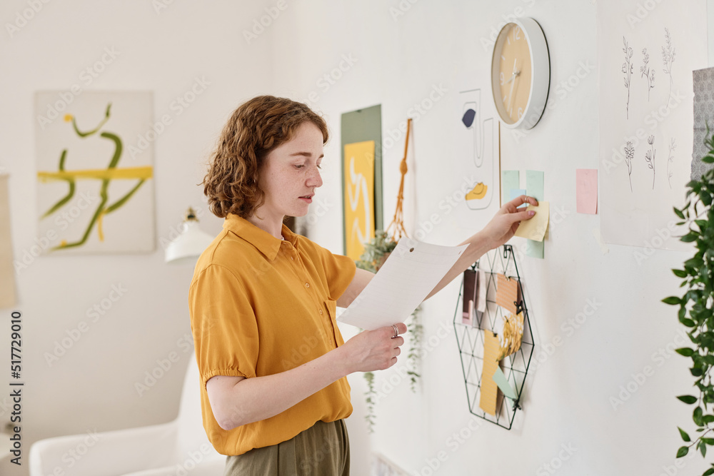 Aufkleber young creative freelancer looking through information in paper document while standing in front of w