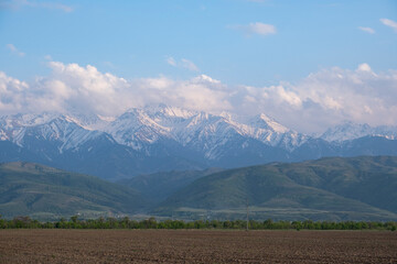 A plowed field against the backdrop of majestic mountains. Landscape of arable land near the mountains.