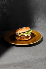 Classic american burger on ceramic plate in dark minimal style. Beef burger on gray stone table with hard shadow. Fast food dark concept. American burger on gray concrete background. Simple food menu.