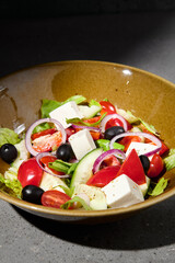 Classic greek salad on ceramic bowl in minimal style. Simple composition with greek salad on gray stone background with hard shadow. Dark concept menu. Vegetable salad on concrete table and shadow.
