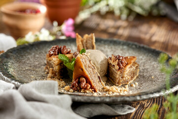 Traditional eastern sweets - baklava with walnuts and ice cream on wooden table. Turkish pastry baklava on modern plate in restaurant menu. Arabic dessert with nuts and honey on wooden background.