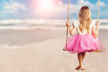 Child tourist swinging on swing, sandy beach. Tropical vacation.