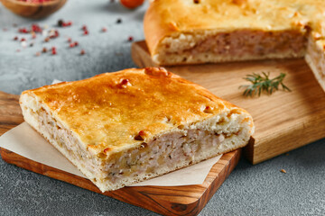 Classic chicken and potato pie on wooden board with ingredients. Composition with chicken pie on concrete background with textile and spices. Homemade pie with turkey and potato in rustic style.